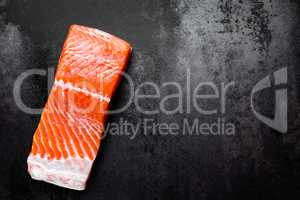 Raw salmon or trout sea fish fillet on black metal background, top view