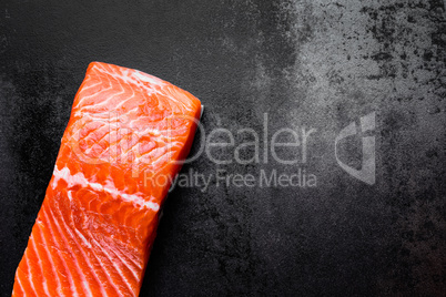 Raw salmon or trout sea fish fillet on black metal background, top view