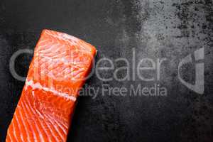 Raw salmon or trout sea fish fillet on black metal background, top view