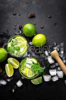 Refreshing mint cocktail mojito with rum and lime, cold drink or beverage with ice on black background, top view