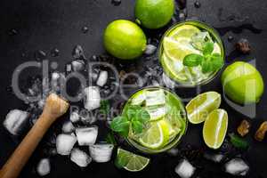 Refreshing mint cocktail mojito with rum and lime, cold drink or beverage with ice on black background, top view