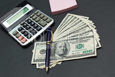 Dollars at black office desk with calculator and pencil