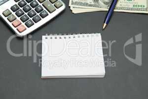 Calculator, Dollars and Notebook on black office desk