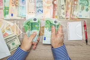 Banker counting Euro at his office table, Empty Notebook World currencies around him