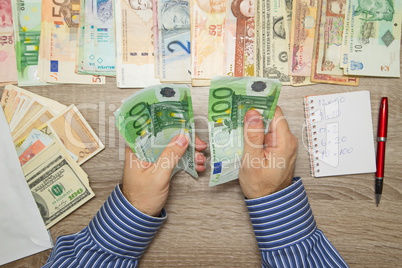 Banker counting Euro at his office table, Empty Notebook World currencies around him