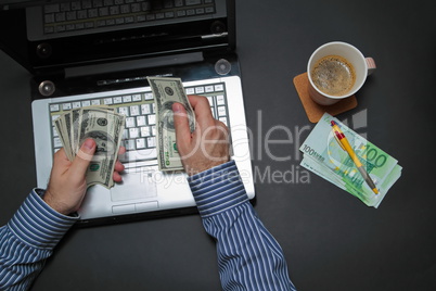 Businessman working on laptop and counting money while as he drinks coffee