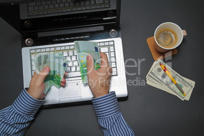 Businessman working on laptop and counting money while as he drinks coffee