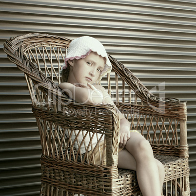 Beautiful small girl seating in wicker chair