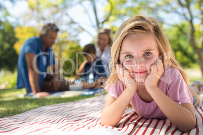 Smiling girl lying on blanket while family sitting in background