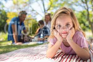 Smiling girl lying on blanket while family sitting in background