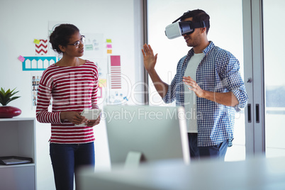 Female colleague assisting businessman while using virtual reality headset