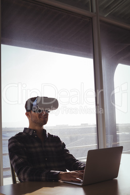 Businessman using virtual reality headset while using laptop in office