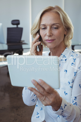 Businesswoman talking on mobile phone while holding digital tablet