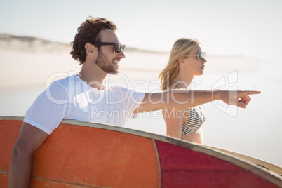 Man with woman gesturing while carrying sunrfboard at beach