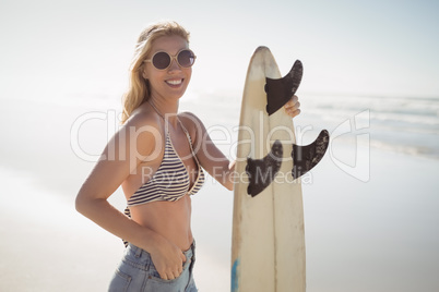 Portrait of happy woman holding surfboard at beach