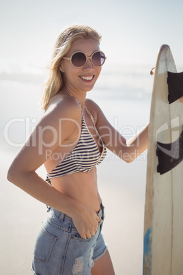 Portrait of smiling young woman holding surfboard at beach