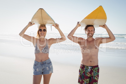 Portrait of happy couple carrying surfboard at beach