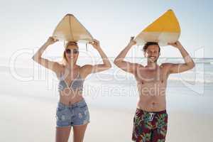 Portrait of happy couple carrying surfboard at beach