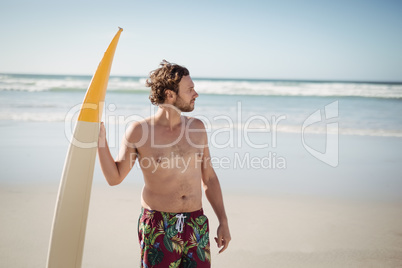 Shirtless man holding surfboard at beach