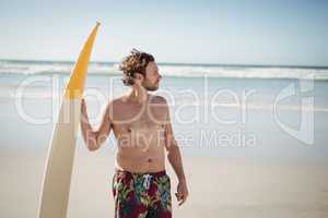 Shirtless man holding surfboard at beach