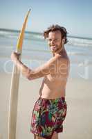 Portrait of happy shirtless man holding surfboard at beach