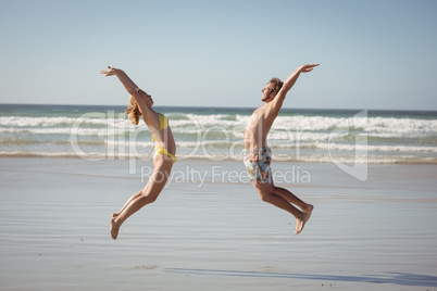 Side view of happy couple jumping on shore at