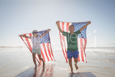 Siblings holding American flags while running at beach