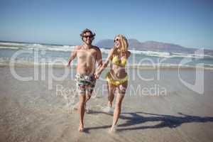 Happy couple holding hands while running on shore