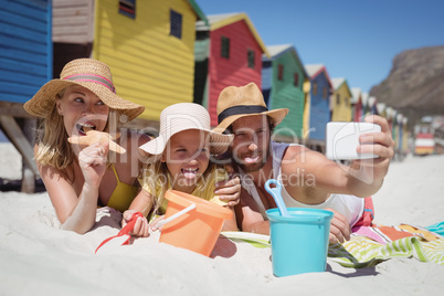 Happy family taking selfie while lying on blanket at beach