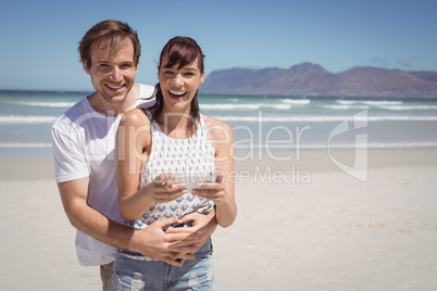 Portrait of cheerful couple holding mobile phone at beach