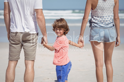 Portrait of boy holding hands with parents at beach