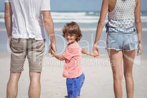 Portrait of boy holding hands with parents at beach