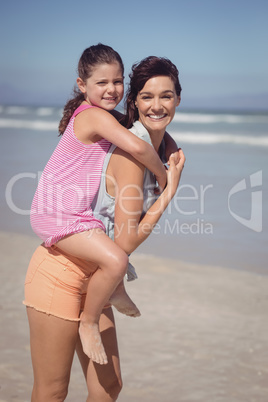 Portrait of smiling mother piggybacking daughter at beach