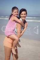 Portrait of smiling mother piggybacking daughter at beach