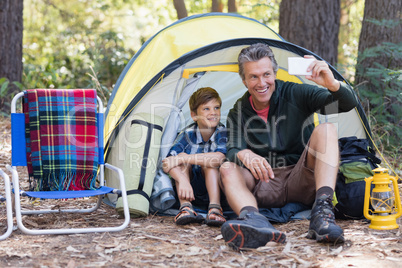 Father and son taking selfie while sitting in tent