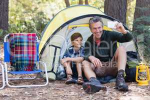 Father and son taking selfie while sitting in tent