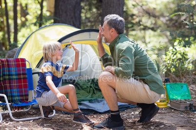 Father and son giving high five by tent at campsite