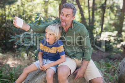 Father and son sticking out tongue while taking selfie in forest