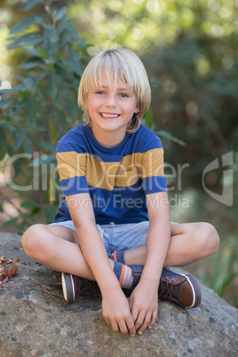 Smiling little boy sitting on rock in forest