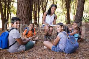 Portrait of happy teacher and students sitting in forest