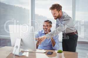 Smiling executives discussing over personal computer at desk