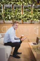 Portrait of smiling executive sitting on sofa and using mobile phone