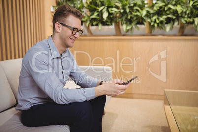 Smiling executive sitting on sofa and using mobile phone