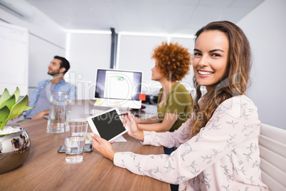 Smiling businesswoman using digital tablet while colleagues discussing in meeting