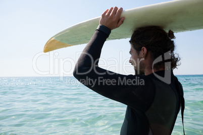 Surfer in wetsuit carrying surfboard over head at beach coast