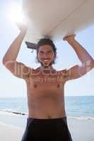 Surfer carrying surfboard over head at beach coast