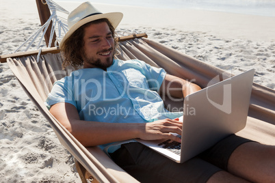 Man relaxing on hammock and using laptop on the beach