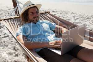 Man relaxing on hammock and using laptop on the beach