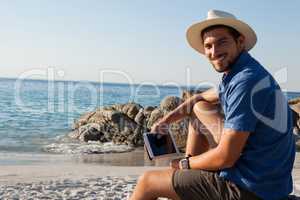 Smiling man with digital tablet sitting on beach