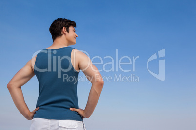 Man standing on beach with hand on hips against blue sky